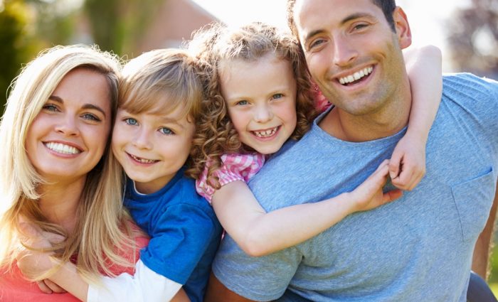 Parents Giving Children Piggyback Rides In Garden Parents Giving Children Piggyback Rides In Garden