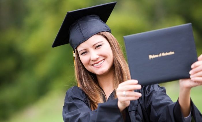 Graduate: Woman Proudly Holding Up Diploma Pretty Asian American woman in black graduatation cap and gown, outdoors.